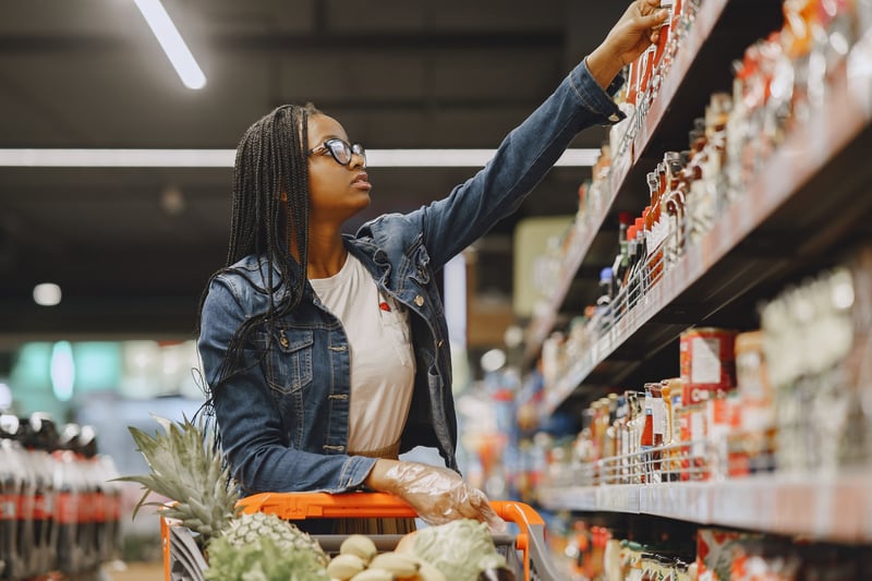 Woman grocery shopping and reaching to grab product off of shelf