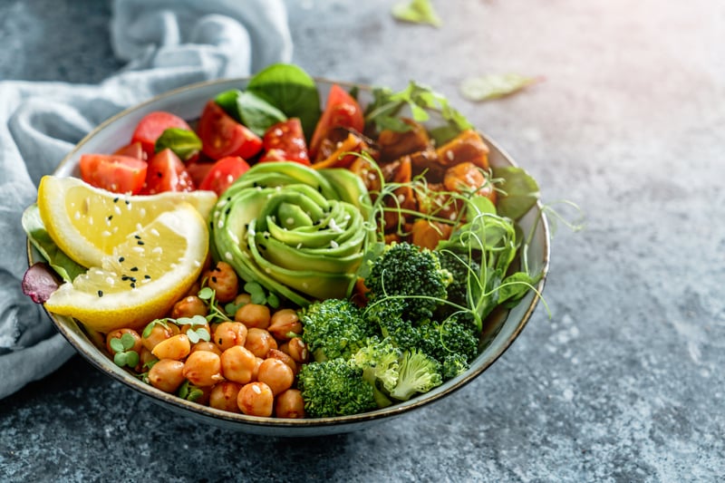 Bowl of plant-based food, featuring avocado, chickpeas, greens and lemon wedge